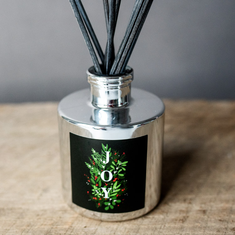 Silver diffuser bottle with black reeds on wood table top.